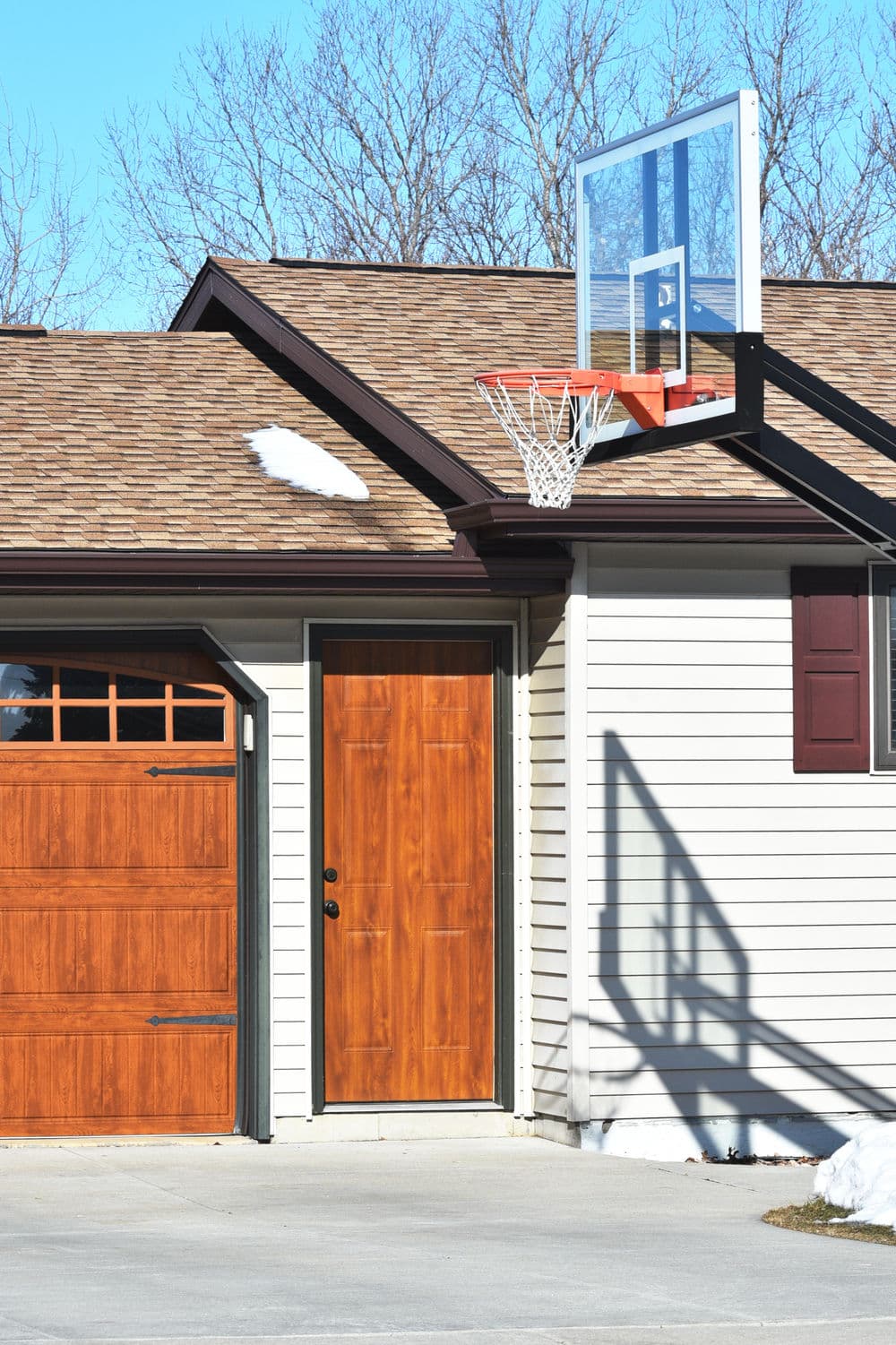 Basketball hoop on garage, wooden door, and driveway in residential setting with clear sky.